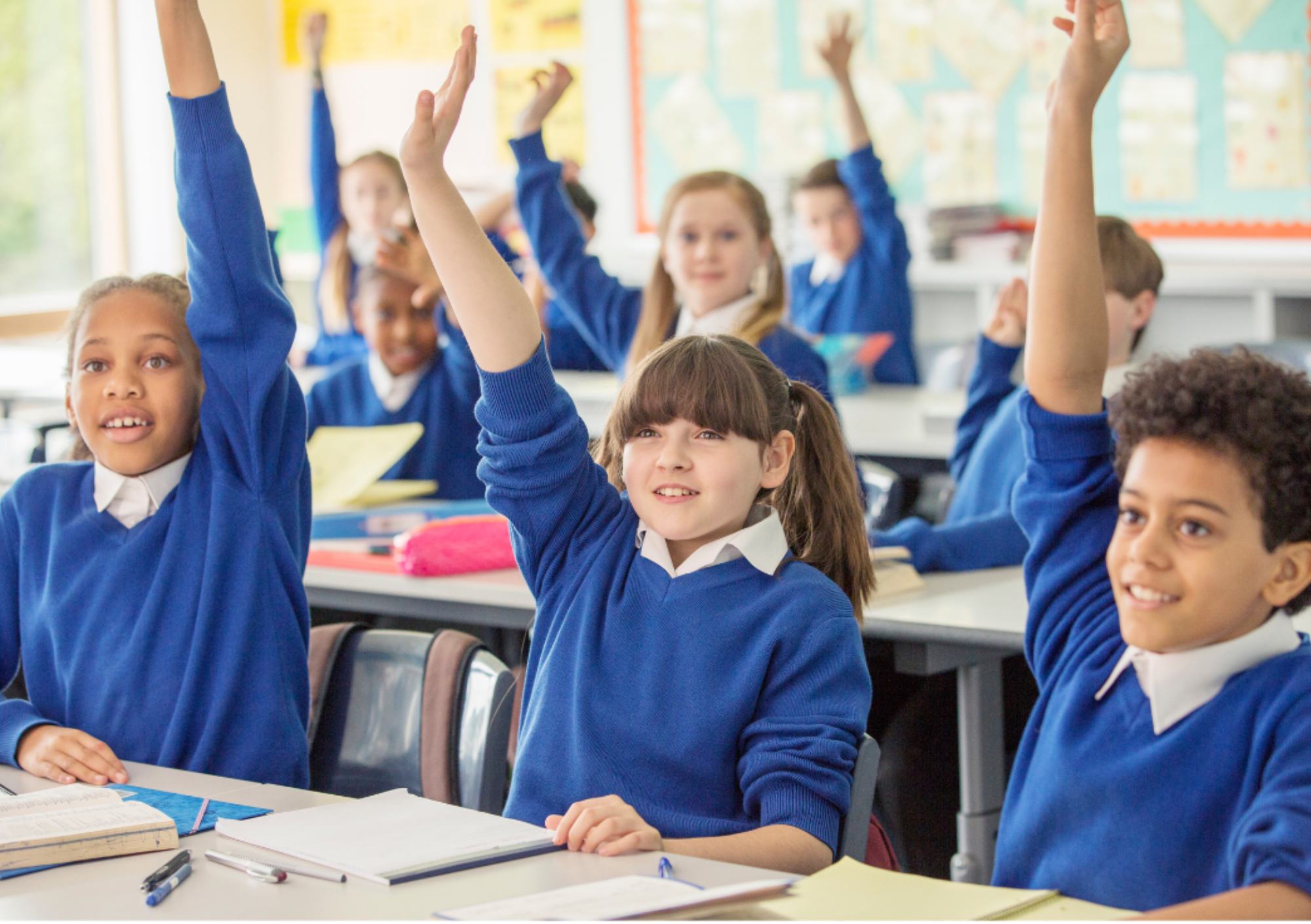 Primary school children with hands raised in class